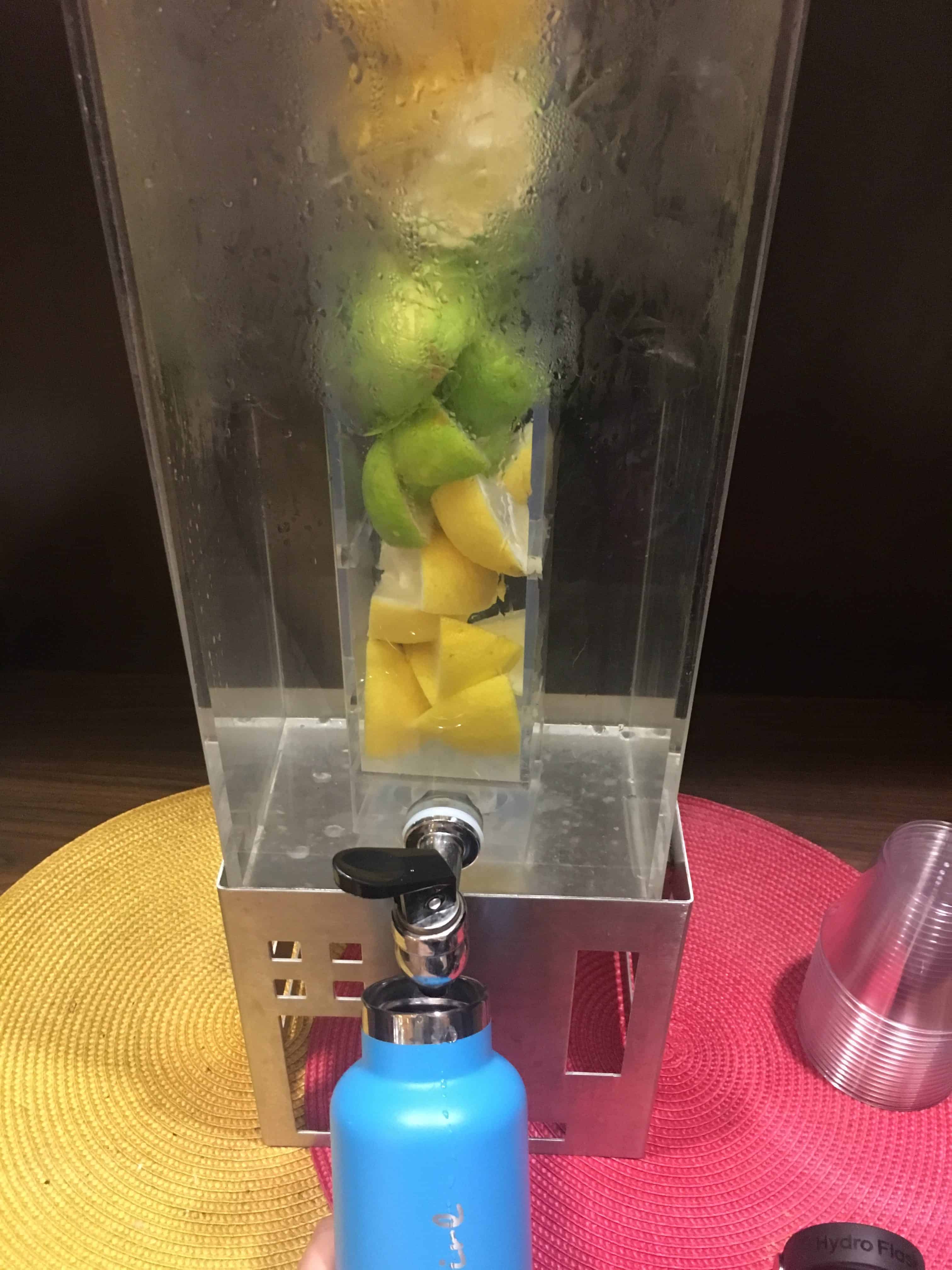 Photo showing author filling blue hydroflask water bottle with water infused with fresh lemons and limes at a Marriott Residence Inn. https://trimazing.com/