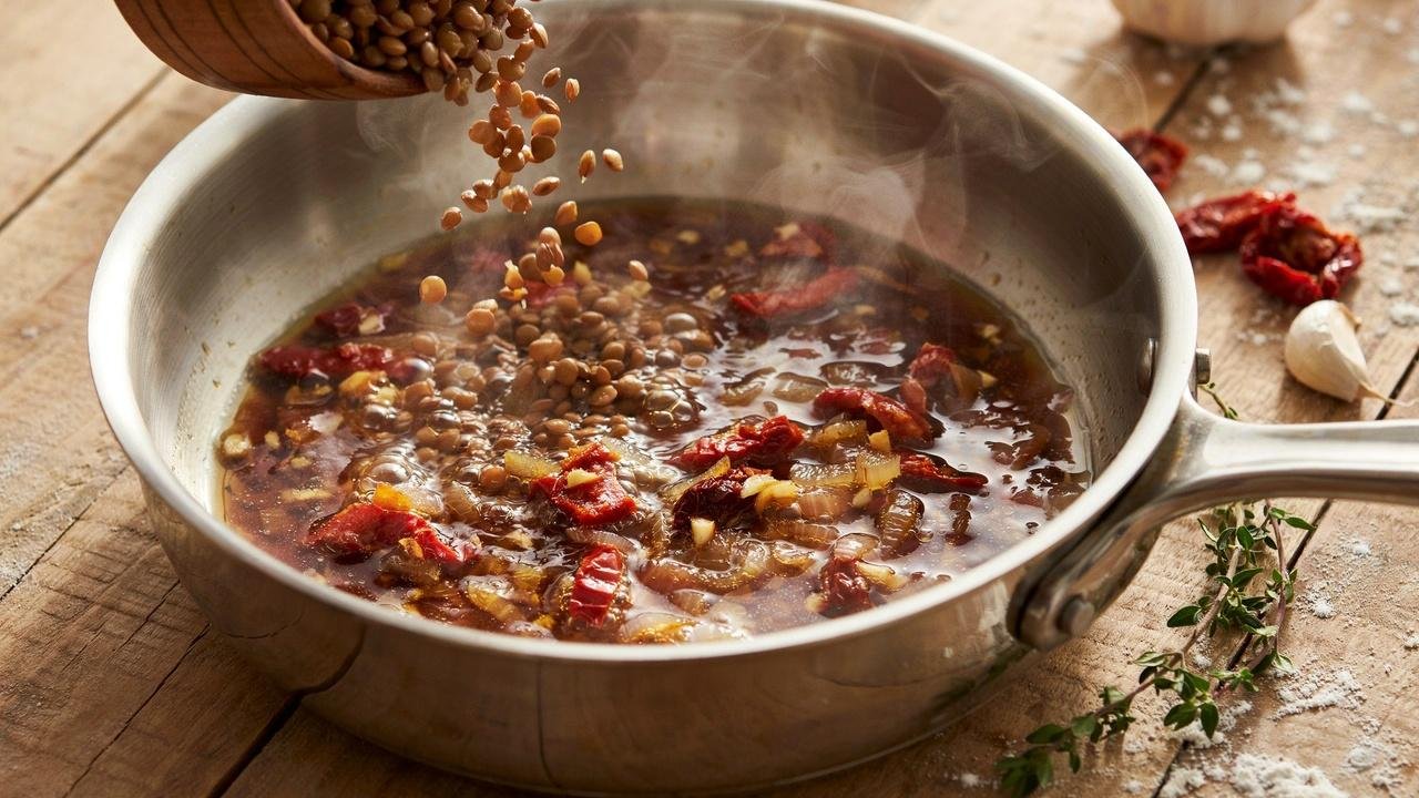Cooked lentils added into simmering sauce with onion, garlic, and sun dried tomatoes.