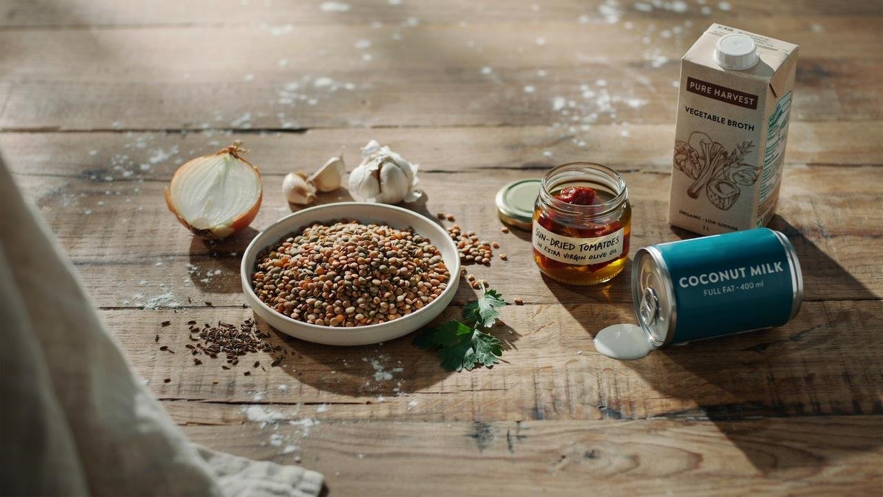 Lentils, onion, garlic, sun dried tomatoes, vegetable broth, and coconut milk on a kitchen counter.