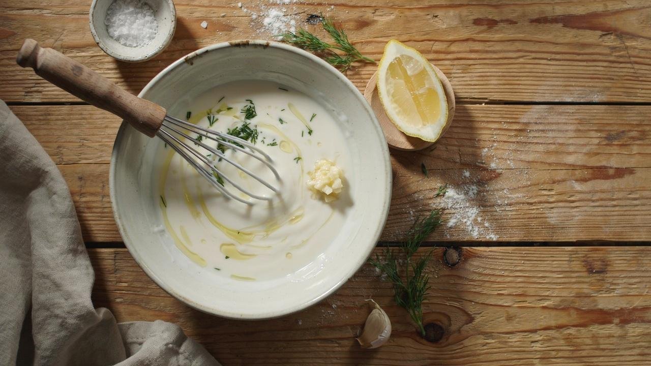 A large ceramic bowl with creamy yogurt dressing being whisked together.