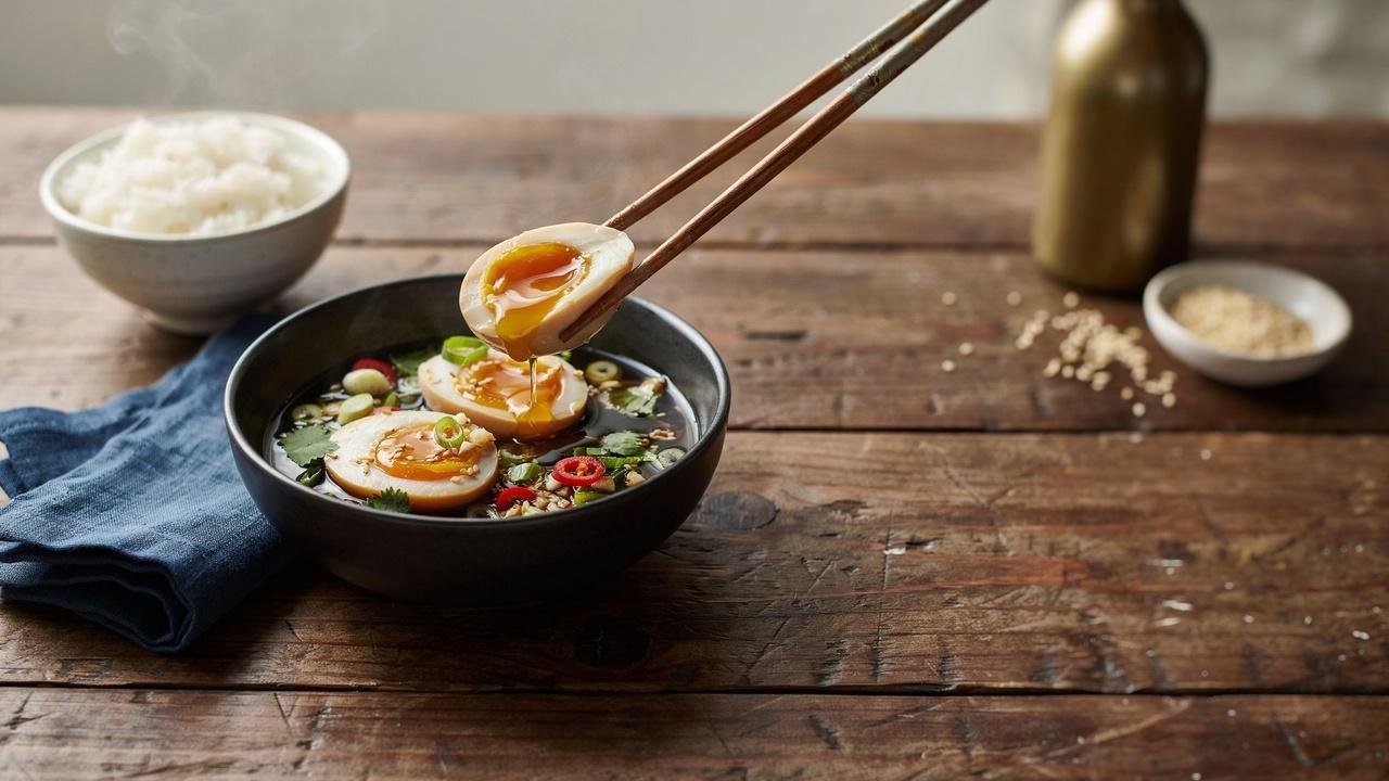 Close-up of authentic Korean drug eggs with jammy yolks in a savory soy marinade, served with rice and garnished with green onions, garlic, sesame seeds, and chili peppers.