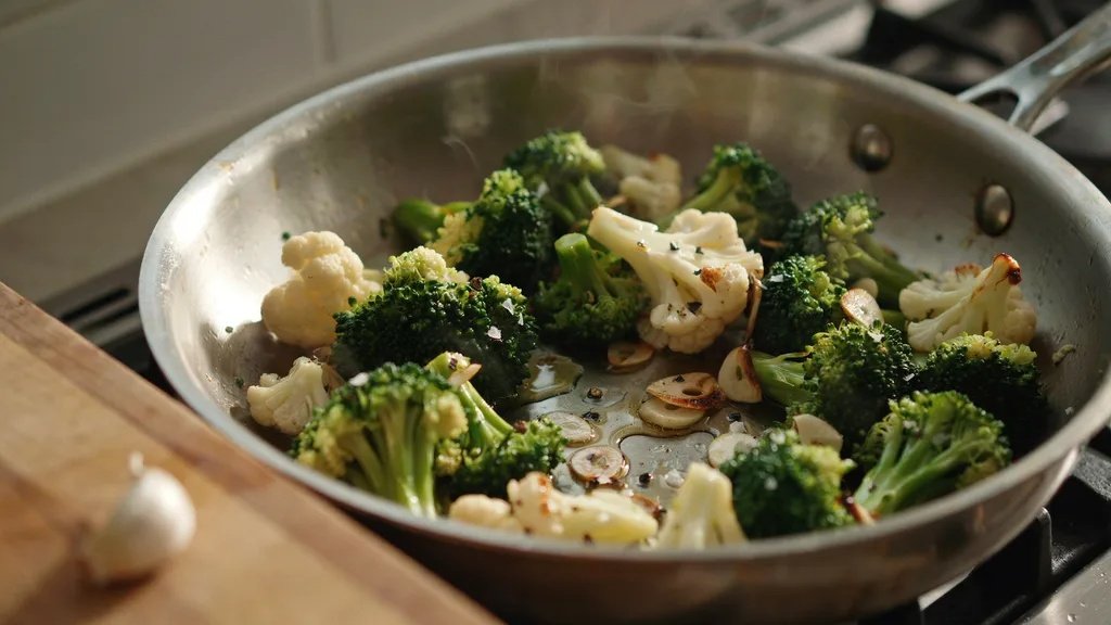 Broccoli and cauliflower cooking with garlic in a skillet.