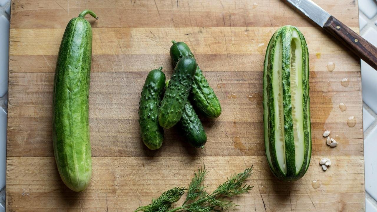English, Persian, and regular cucumbers on a wooden board, ready for slicing.