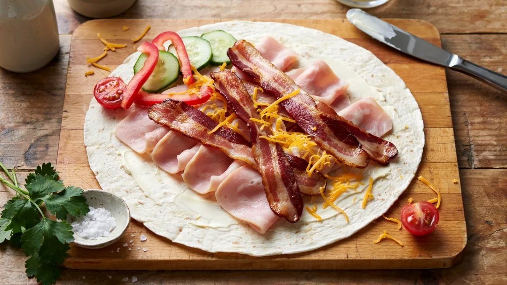 Assembling keto pinwheel ingredients on a tortilla.