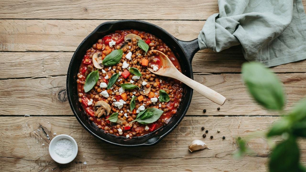 Overhead view of Marry Me Lentils in a skillet with creamy tomato sauce, diced carrots, mushrooms, bell peppers, and fresh basil on top.