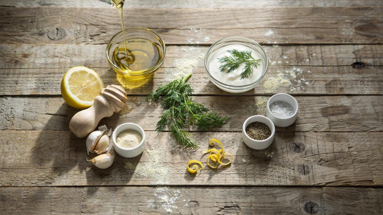 Small glass bowl of golden olive oil, fresh lemon halves, whole garlic cloves and a small dish of garlic powder, a tiny bowl of sea salt and cracked black pepper.