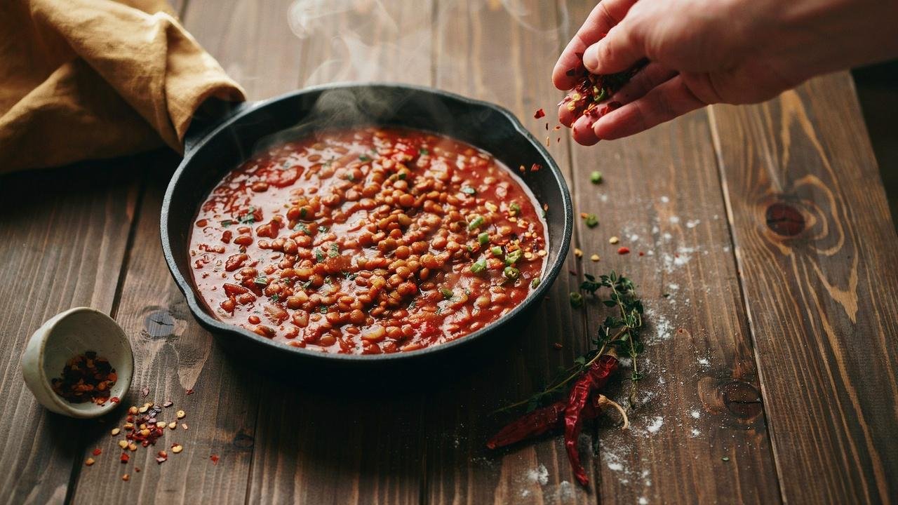 Creamy Marry Me lentils in a skillet with chili flakes and chopped green chilies being sprinkled on top.