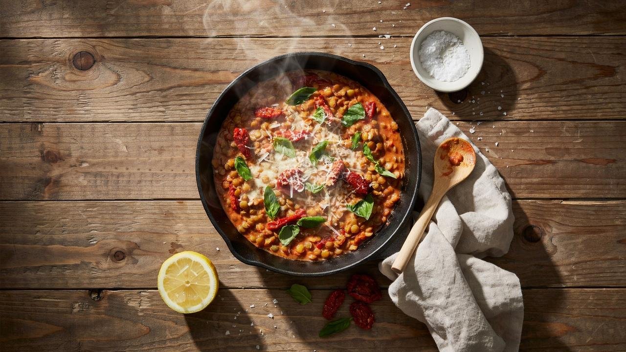 Creamy Marry Me Lentils in a cast iron skillet with basil, parmesan, and sun-dried tomato sauce.