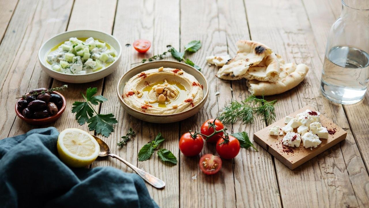 Cucumber dill yogurt salad served with hummus, pita bread, olives, and tomatoes on a wooden table.