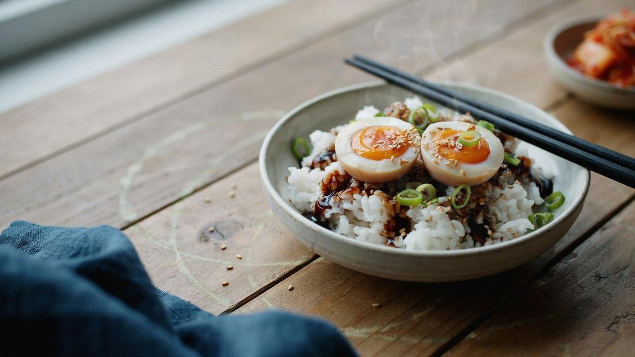 Korean drug eggs with jammy yolks served over steamed rice and garnished with green onions and sesame seeds.