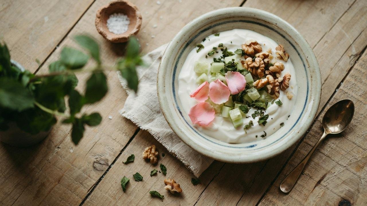 A bowl of Persian Mast-o-Khiar, creamy yogurt cucumber salad, diced cucumbers, dried mint sprinkled on top, garnished with walnuts and rose petals.