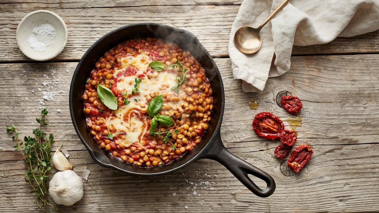 Creamy Marry Me Lentils with parmesan and basil in a cast iron skillet on a wooden table.