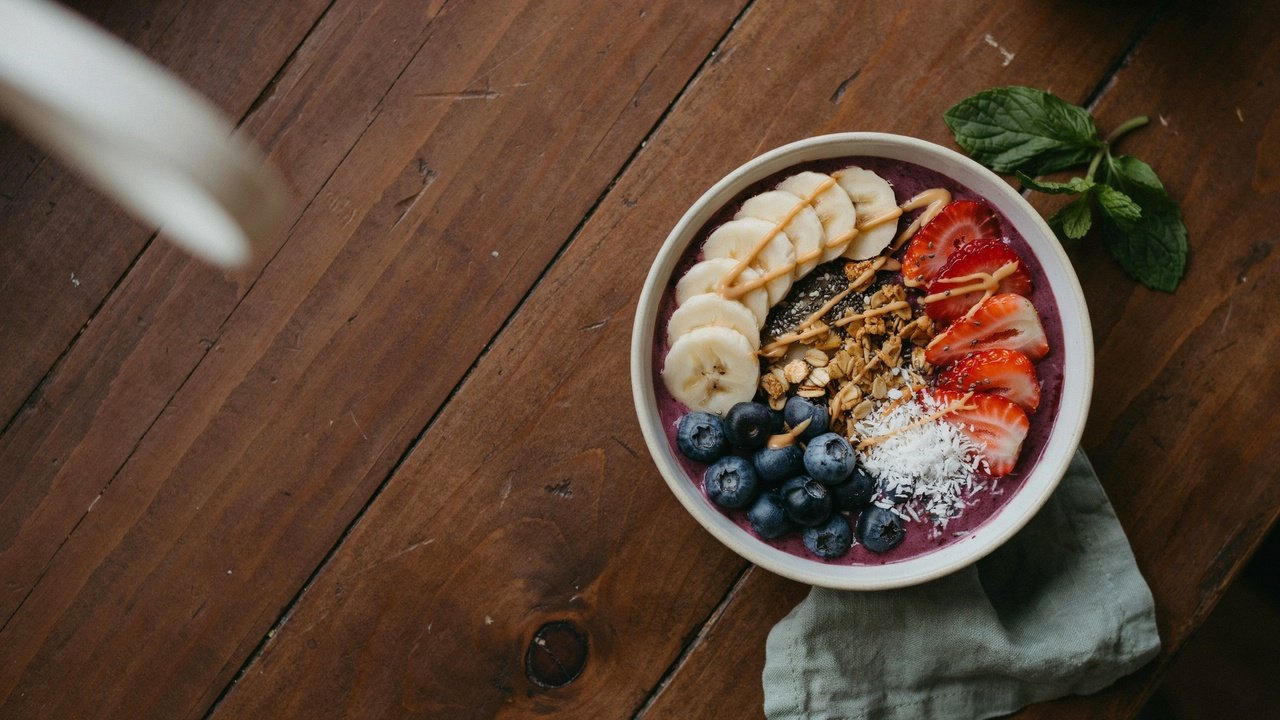 Vegan acai bowl topped with banana, berries, granola, chia seeds, coconut flakes, and almond butter drizzle.