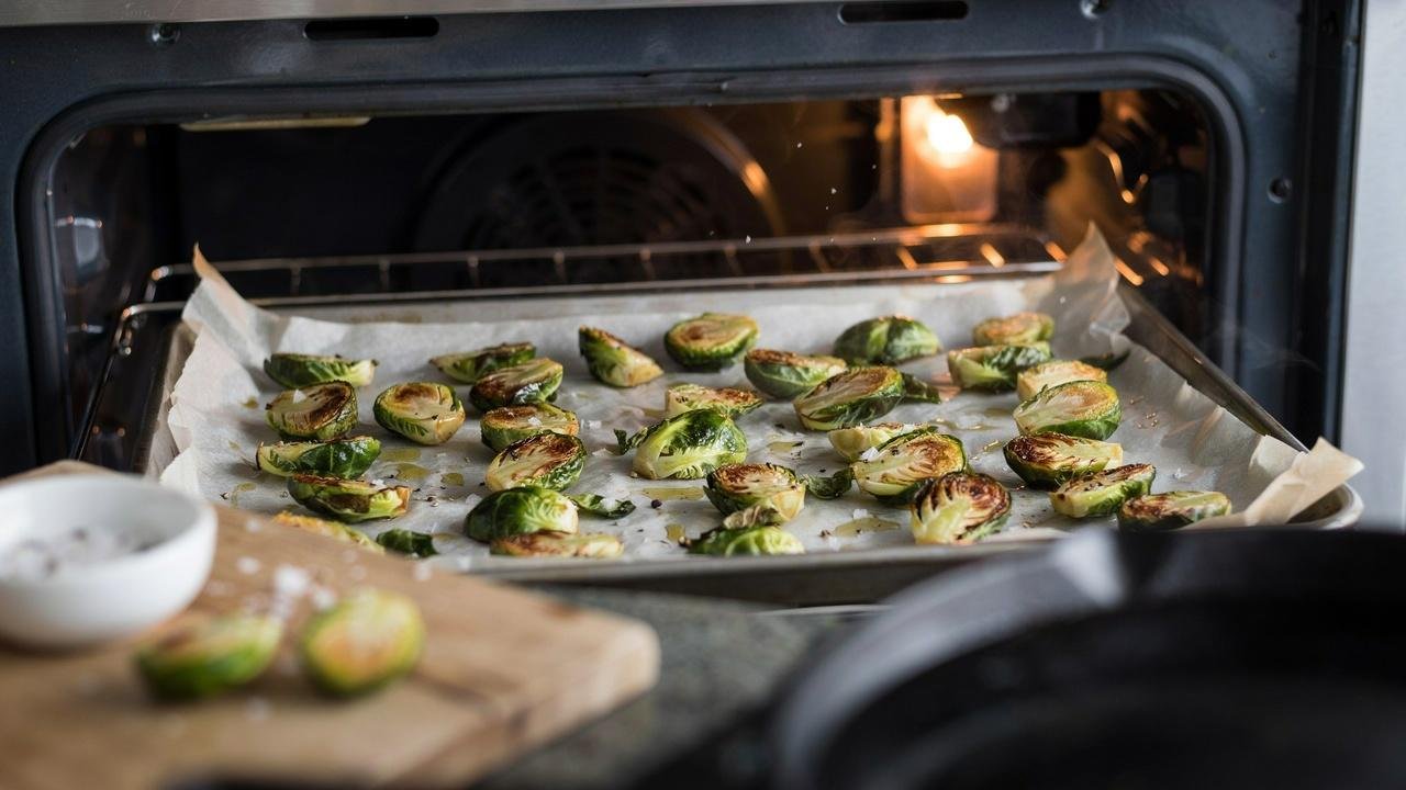 Seasoned Brussels sprouts spread on a baking tray, roasting until golden brown with crispy caramelized edges.