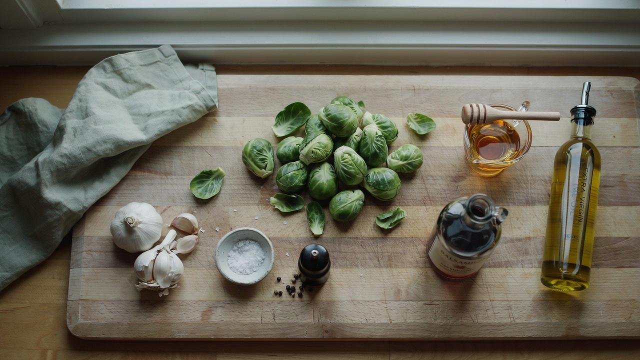 Fresh ingredients including Brussels sprouts, honey, balsamic vinegar, garlic, and olive oil prepared for making a sweet and tangy side dish.