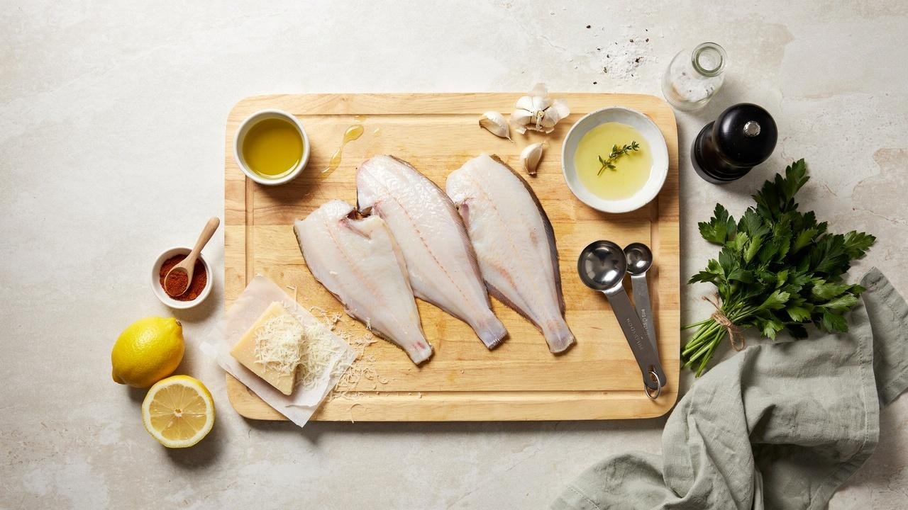 Ingredients for baked flounder including fresh fillets, garlic, lemon, Parmesan, butter, and seasonings.