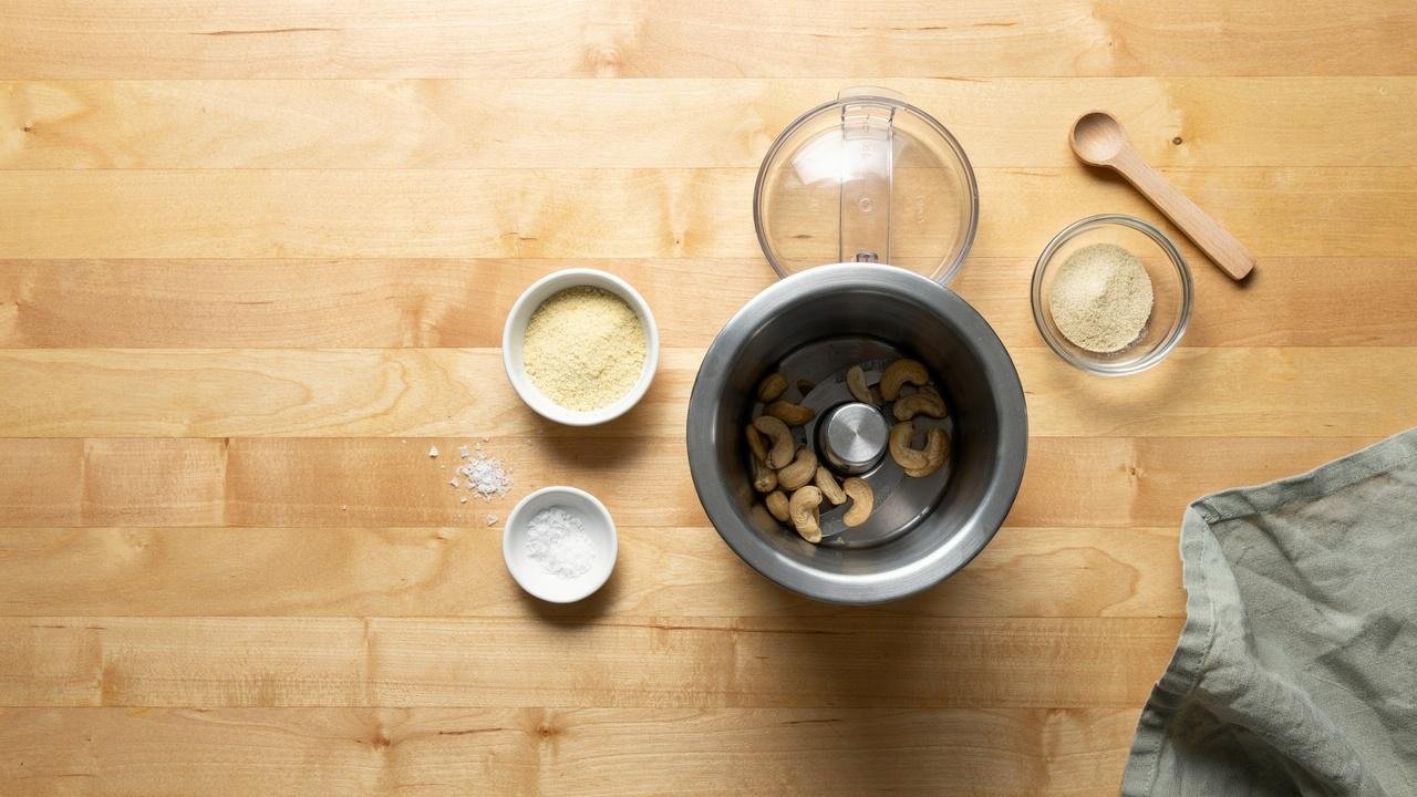 Measured raw cashews, nutritional yeast, garlic powder, and salt prepared in a food processor before blending.