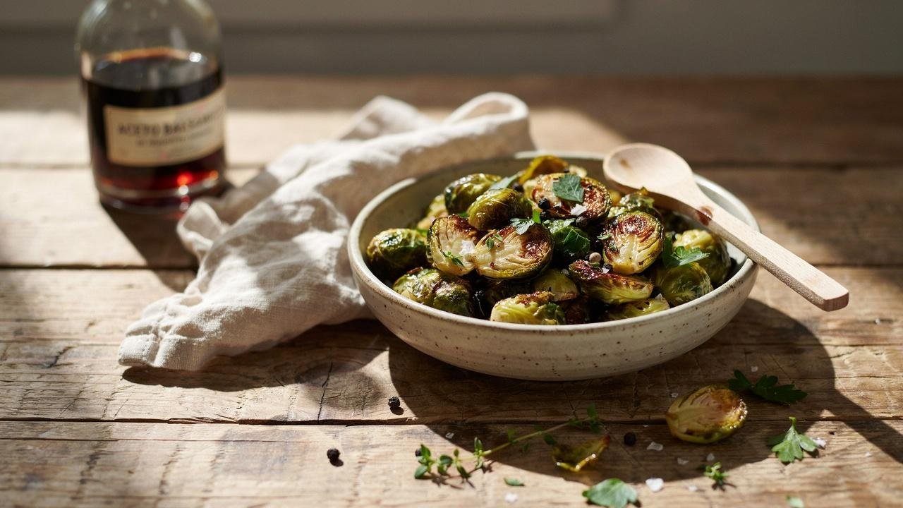 Bowl of crispy honey balsamic Brussels sprouts with caramelized edges, glossy glaze, and fresh herbs served as a flavorful side dish.