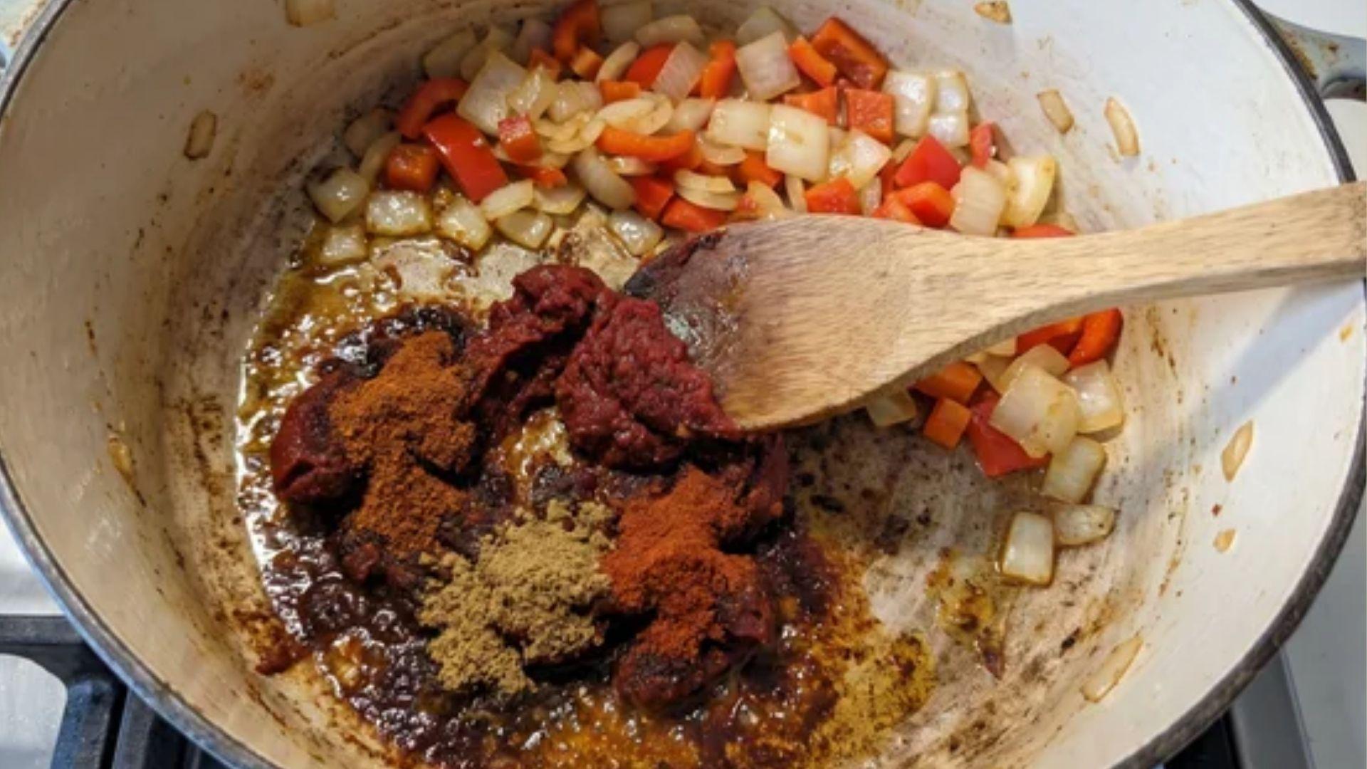 Tomato paste and chili spices cooking with vegetables in a Dutch oven