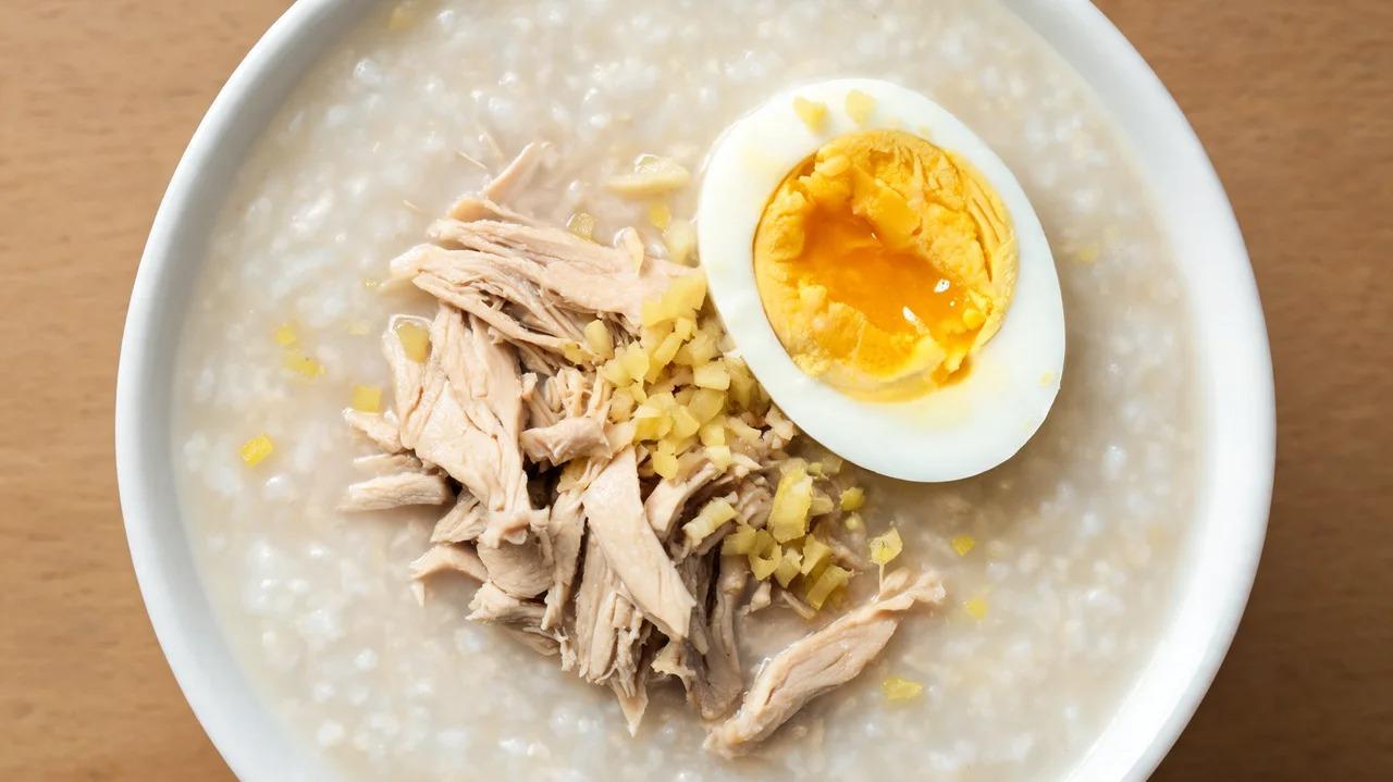 Bowl of congee topped with shredded chicken, soft-boiled egg, and minced ginger
