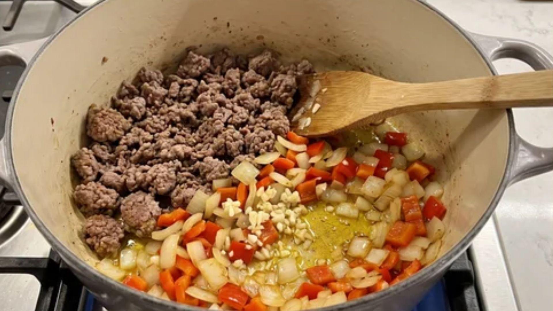 Onion, bell pepper, garlic, and browned meat cooking in a Dutch oven