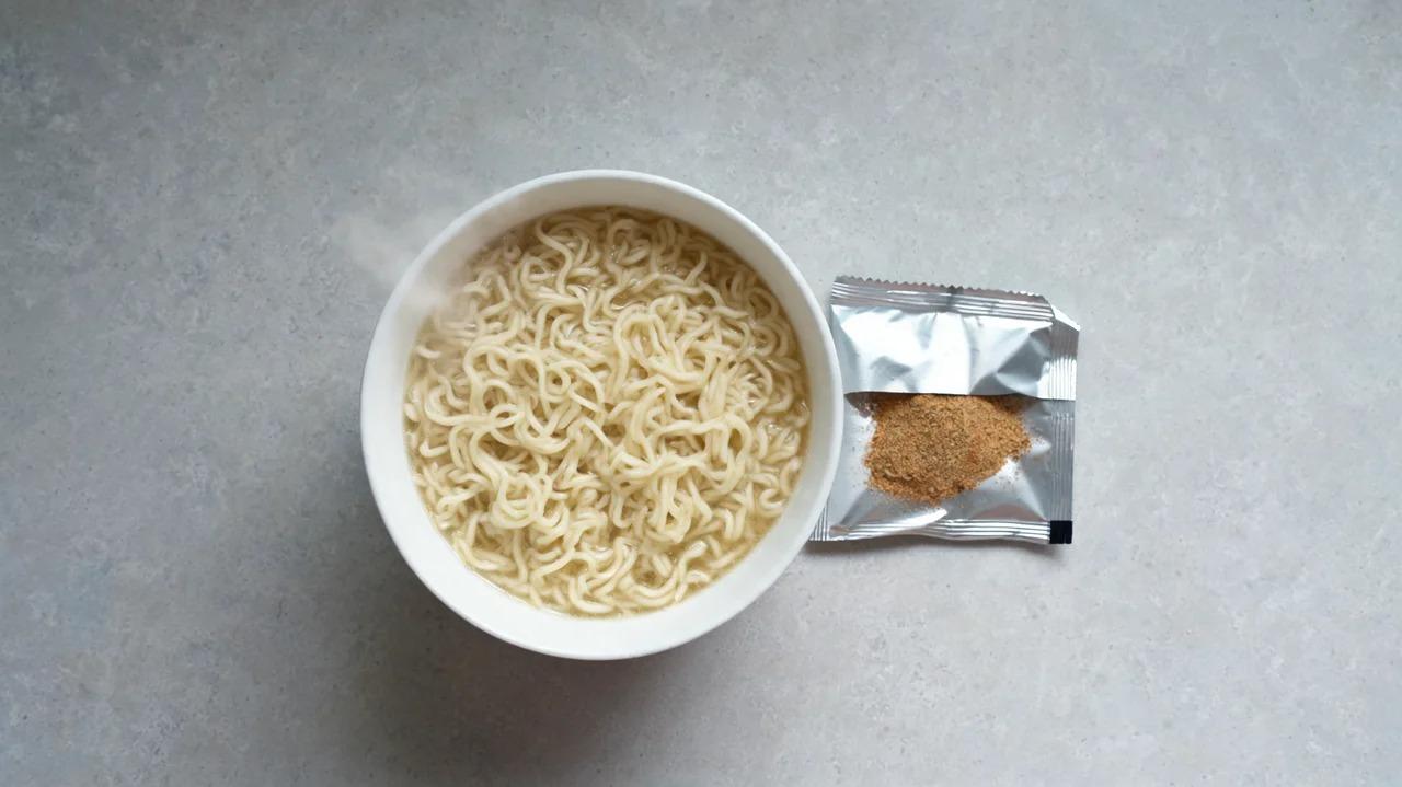Cooked instant noodles with a flavour packet beside the bowl