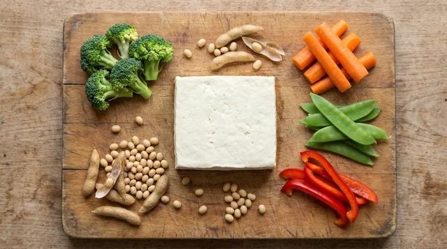 Plain tofu block with soybeans, broccoli, and vegetables on a kitchen surface