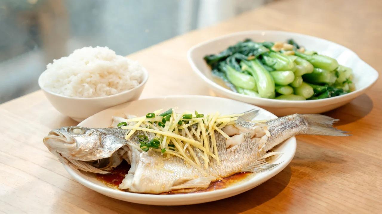 Steamed fish with ginger and scallion, garlic bok choy, and steamed rice on a table