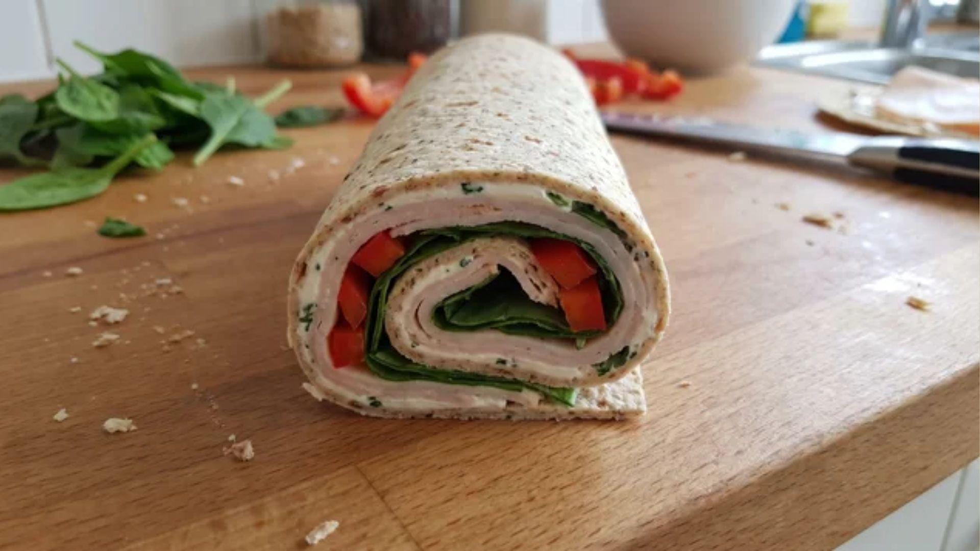 Filled tortilla rolled into a tight log with cream cheese, turkey, and cheese layers