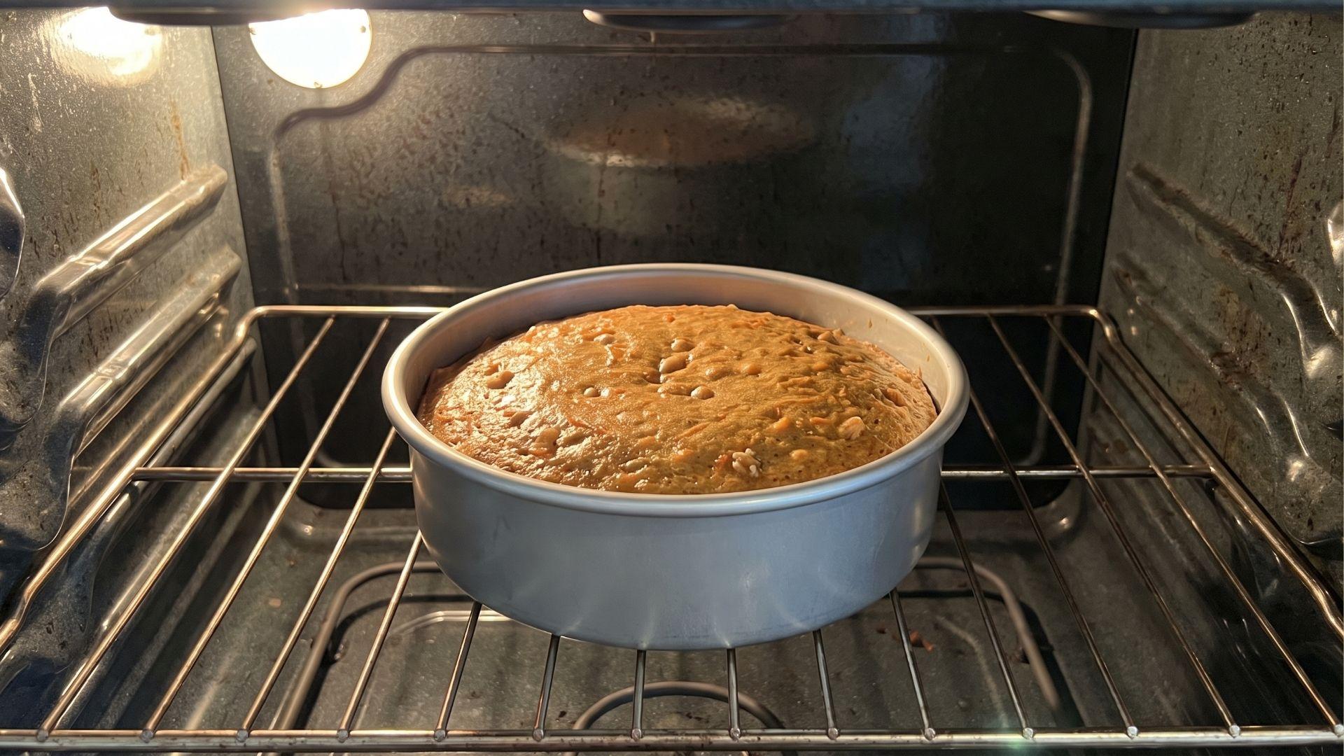 Small carrot cake baking in a 6-inch round pan inside an oven